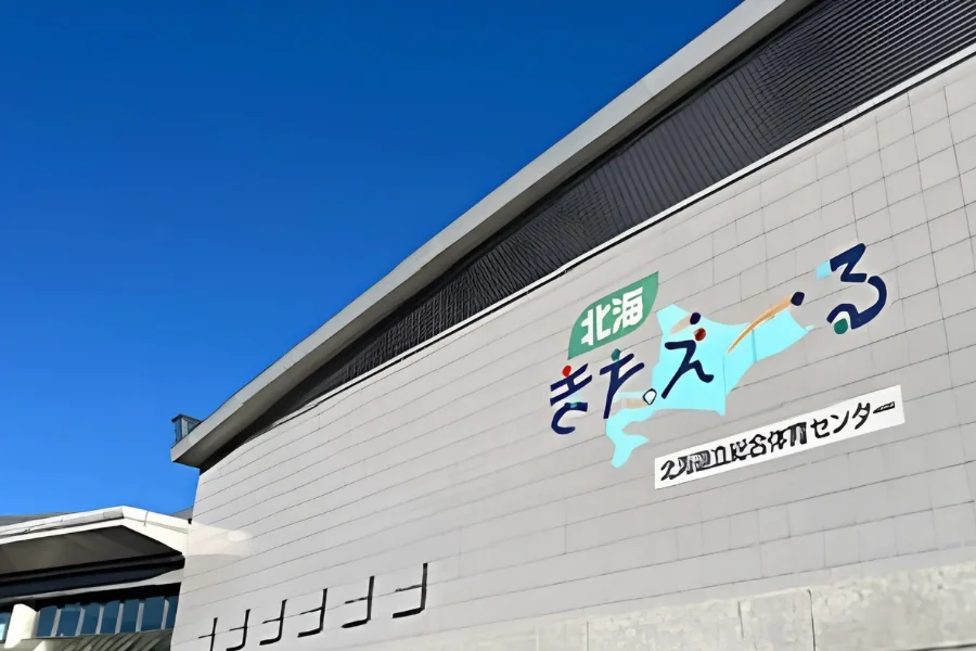 北海きたえーるの外観。青空の下、灰色の壁面に「北海きたえーる 北海道立総合体育センター」のロゴが大きく描かれている