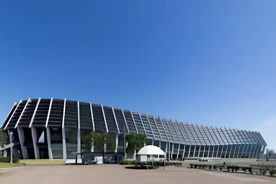 ポートメッセなごや第1展示館の外観。白い柱が櫛のように並ぶ曲面の屋根が横に長くのび、下部はガラス張りになっている。手前に広い舗装の広場がある