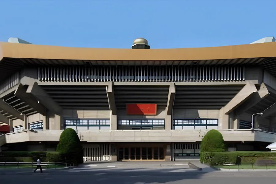 日本武道館の外観。青空の下、反りのある大きな屋根の下にコンクリートの柱が並び、正面中央に赤い扁額が掛かっている